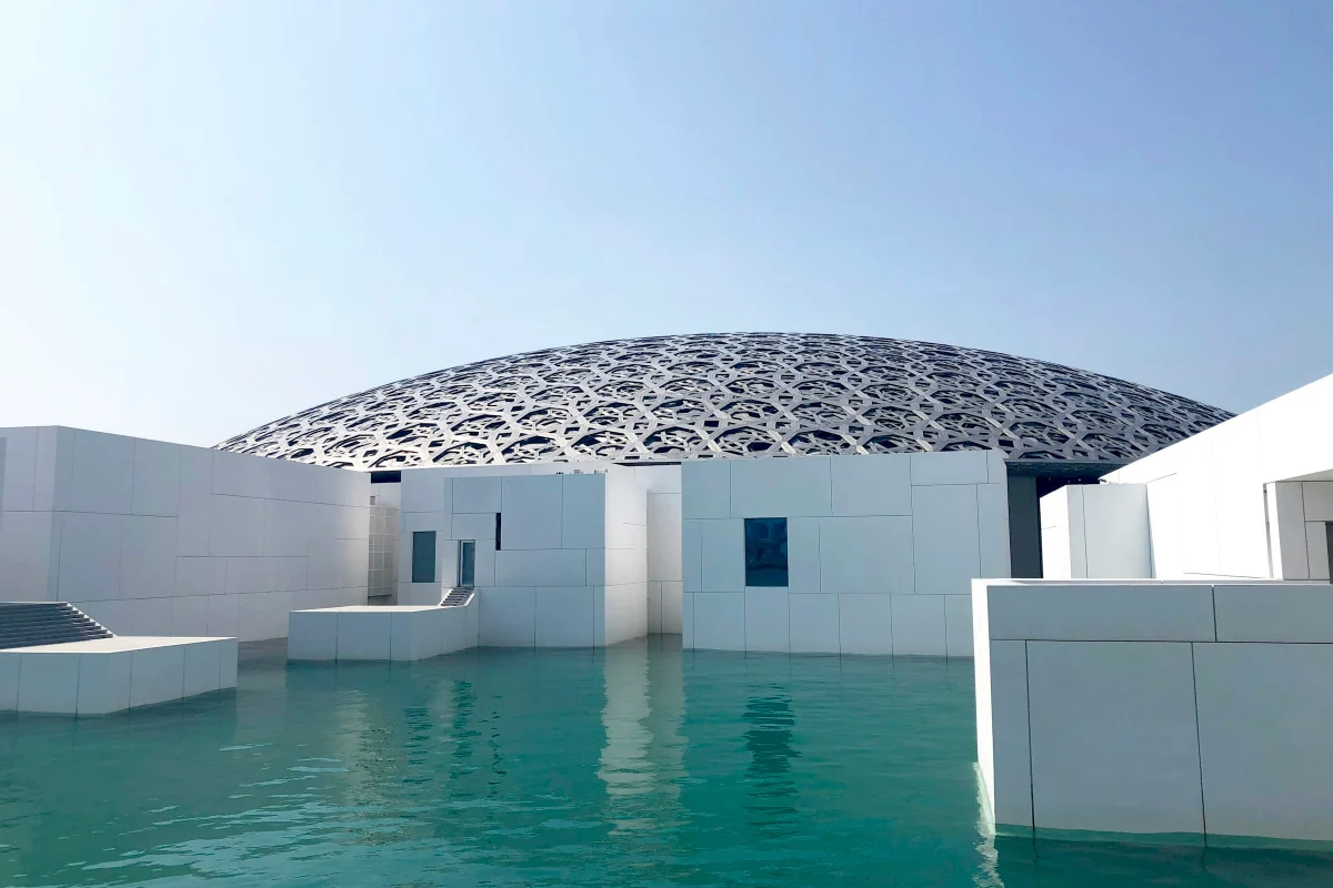 Louvre Abu Dhabi dome above white museum buildings and still turquoise water on Saadiyat Island
