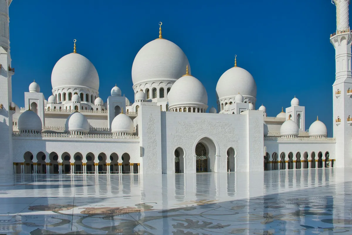 White marble domes and arches of Sheikh Zayed Grand Mosque in Abu Dhabi under a deep blue sky
